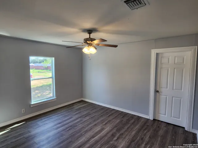 an empty room with wooden floor chandelier fan and windows