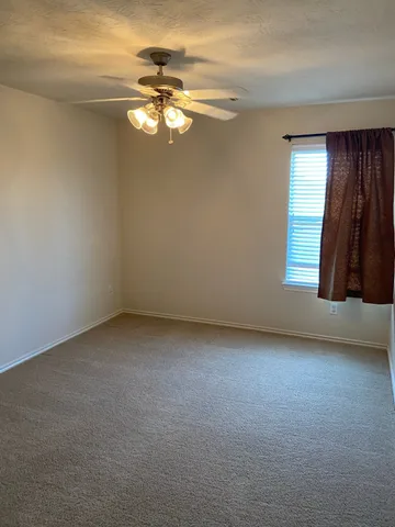 a view of an empty room with window and chandelier fan