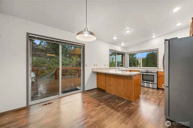 a kitchen with stainless steel appliances granite countertop a refrigerator a sink dishwasher a oven and a large window with wooden floor