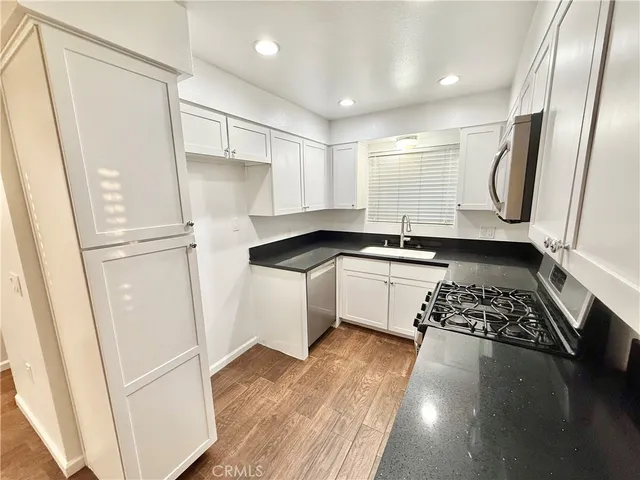 a kitchen with granite countertop a refrigerator a sink and white cabinets