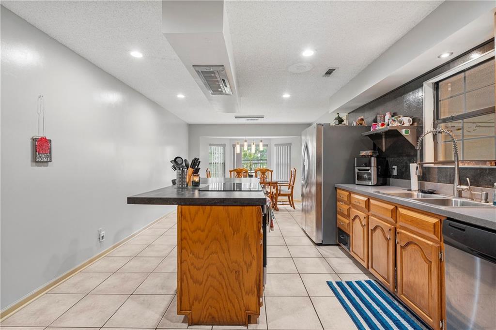 1065 5 Mile Road Eufaula, AL 36027 - Photo 7 of 28 Kitchen featuring a textured ceiling, brown cabinets, stainless steel appliances, light tile patterned floors, and a kitchen island