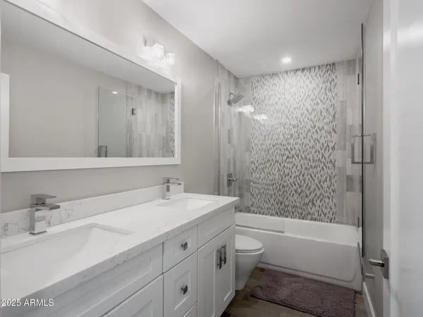 a bathroom with a bathtub shower sink vanity mirror and toilet