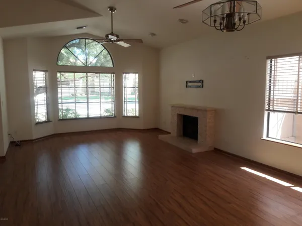 an empty room with wooden floor chandelier and windows