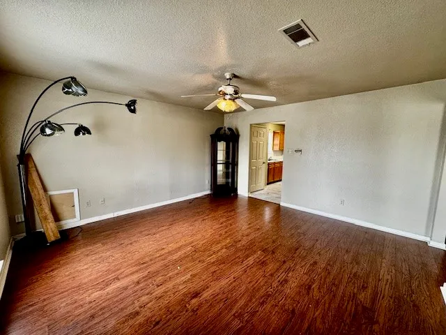 an empty room with wooden floor chandelier fan and windows