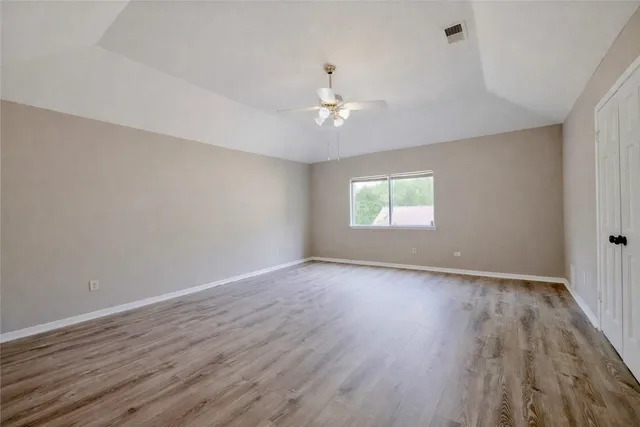 an empty room with wooden floor chandelier fan and windows