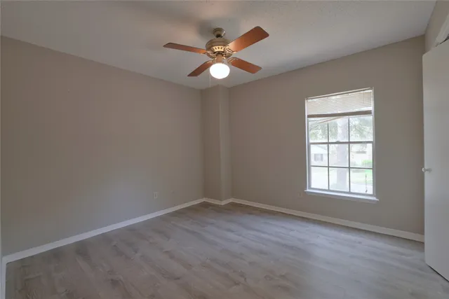 an empty room with wooden floor fan and windows