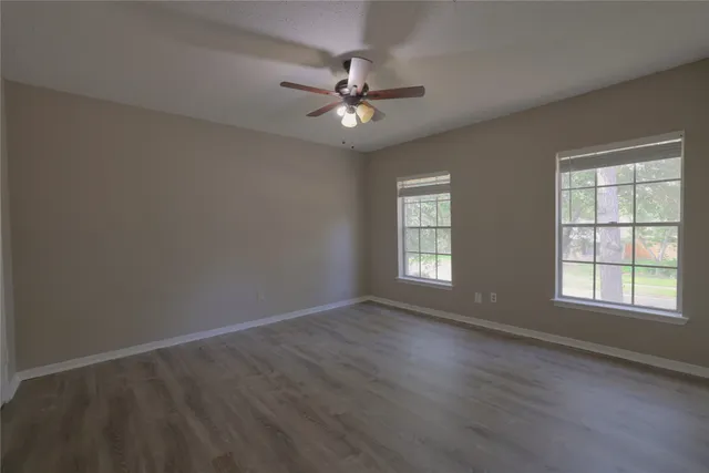 an empty room with wooden floor fan and windows