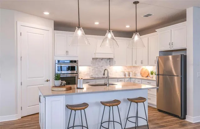 a kitchen with stainless steel appliances granite countertop a refrigerator a sink dishwasher a stove a dining table and chairs with wooden floor