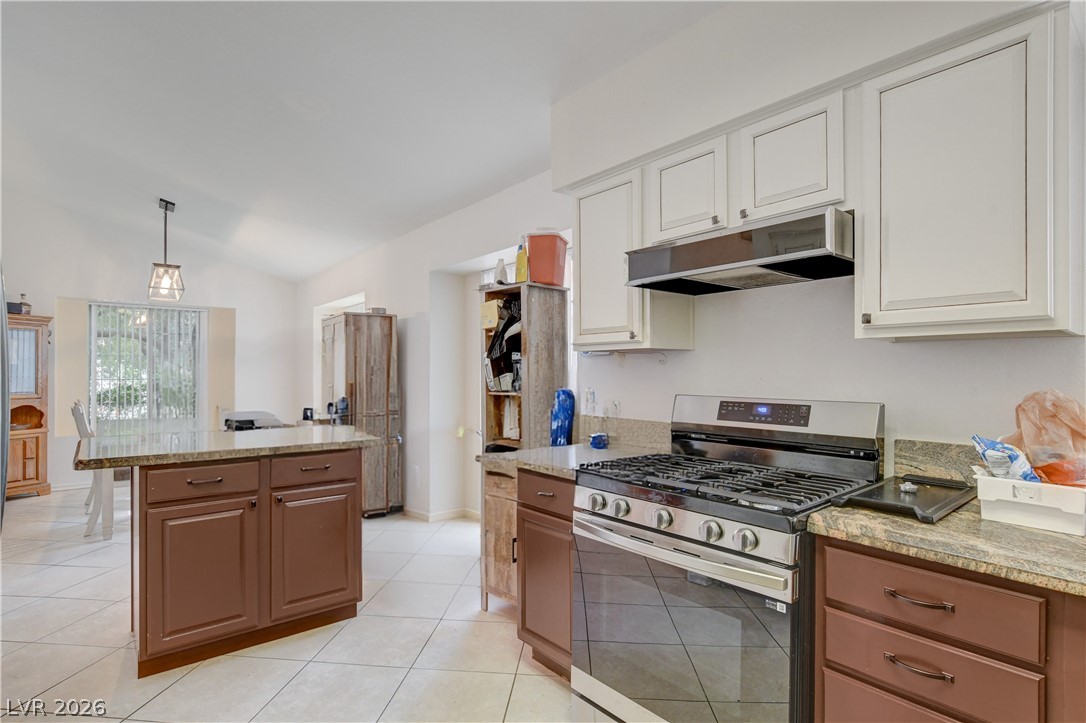 337 Washoe Way Henderson, NV 89074 - Photo 8 of 20 Dual tone kitchen with stainless steel gas range, decorative light fixtures, light tile patterned flooring, light stone counters, and vaulted ceiling