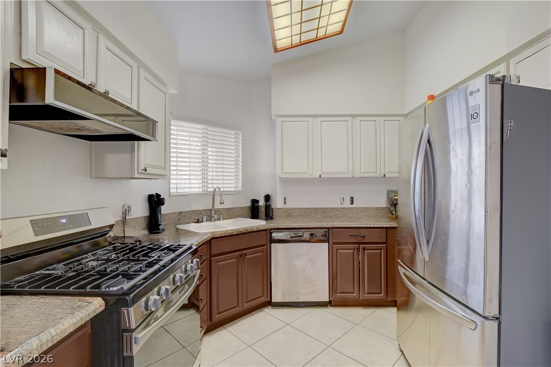 337 Washoe Way Henderson, NV 89074 - Photo 9 of 20 Kitchen with stainless steel appliances, two tone cabinetry, light tile patterned floors, light stone counters, and lofted ceiling