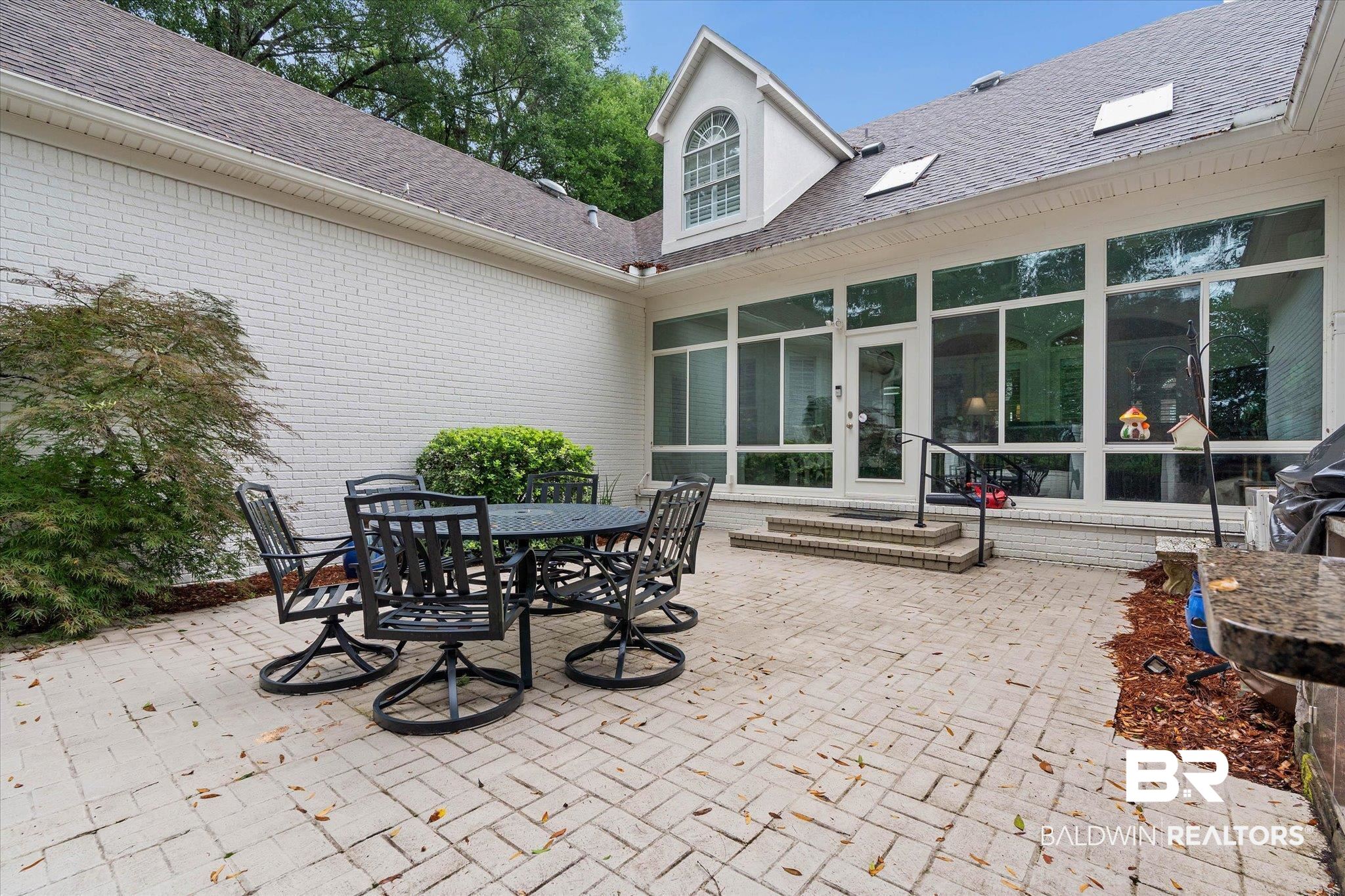 136 Old Mill Road Fairhope, AL 36532 - Photo 27 of 36 Expansive brick paver patio featuring a white painted brick exterior, full-height windows, a dormer with an arched window, and two skylights