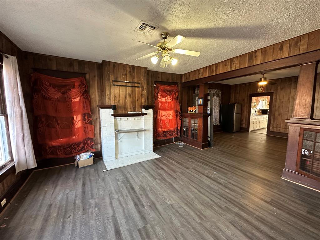 1824 Lyle Avenue Waco, TX 76708 - Photo 4 of 13 Unfurnished living room featuring wood walls, ceiling fan, a textured ceiling, and dark wood-style floors