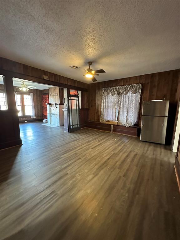 1824 Lyle Avenue Waco, TX 76708 - Photo 6 of 13 Unfurnished living room featuring a ceiling fan, wooden walls, dark wood finished floors, and a textured ceiling