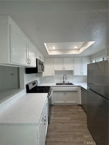 a kitchen with stainless steel appliances granite countertop a stove top oven a sink a refrigerator white cabinets and wooden floor