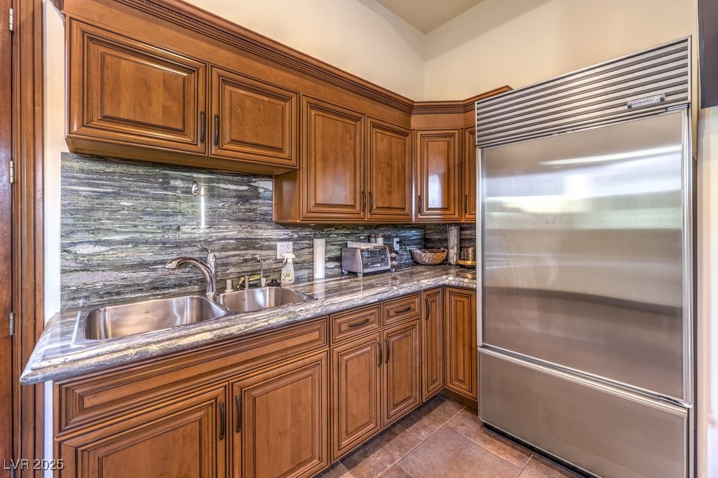 2780 El Camino Road Las Vegas, NV 89146 - Photo 73 of 90 Kitchen featuring a sink, brown cabinetry, built in fridge, dark stone counters, and decorative backsplash