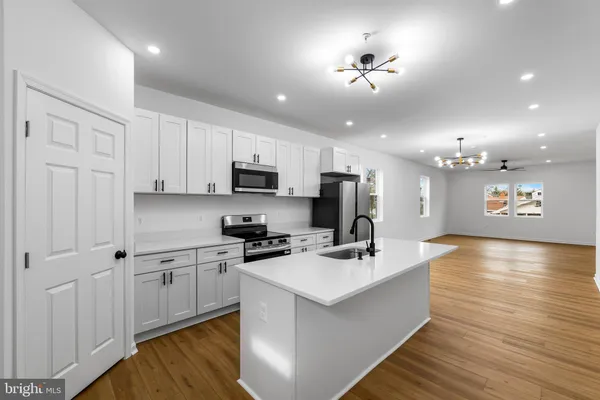 a large white kitchen with kitchen island a sink dishwasher a stove a refrigerator and white cabinets with wooden floor