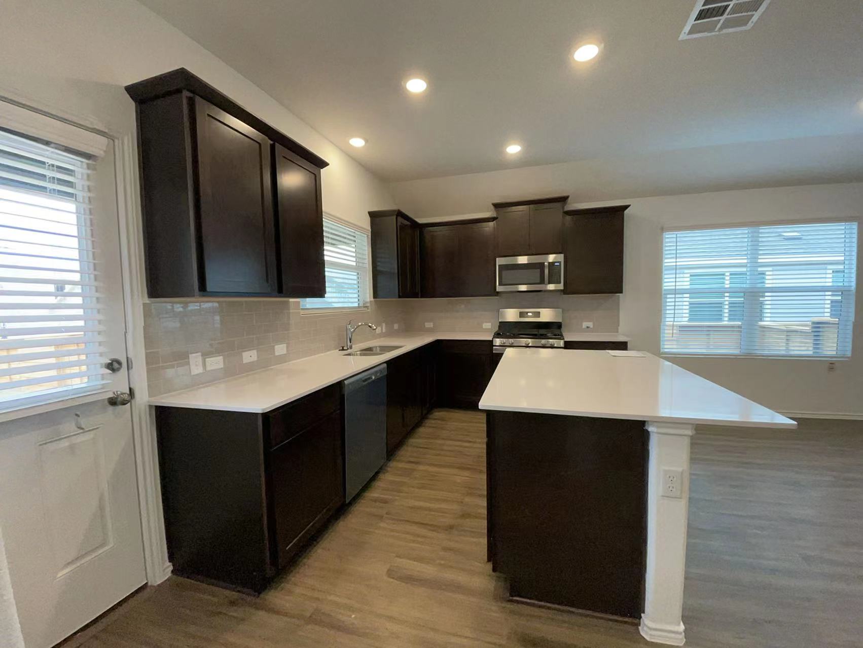 125 Madrid Kyle, TX 78640 - Photo 6 of 23 Kitchen featuring dark wood finish cabinets, a center island, stainless steel appliances, dark wood-style flooring, and tasteful backsplash