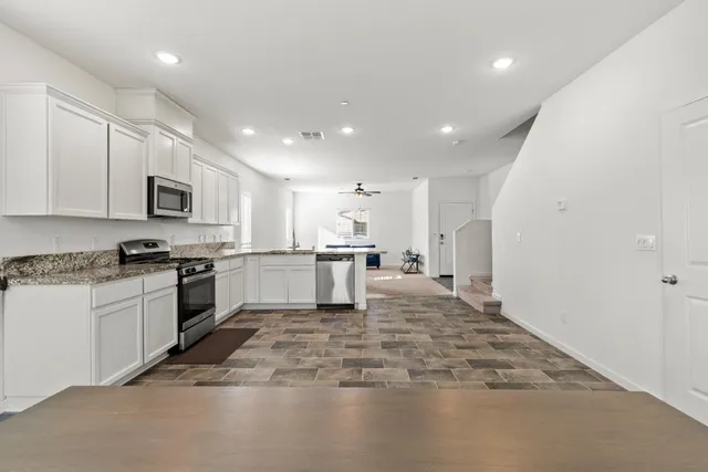 a large kitchen with kitchen island a stove a sink dishwasher a refrigerator and white cabinets with wooden floor