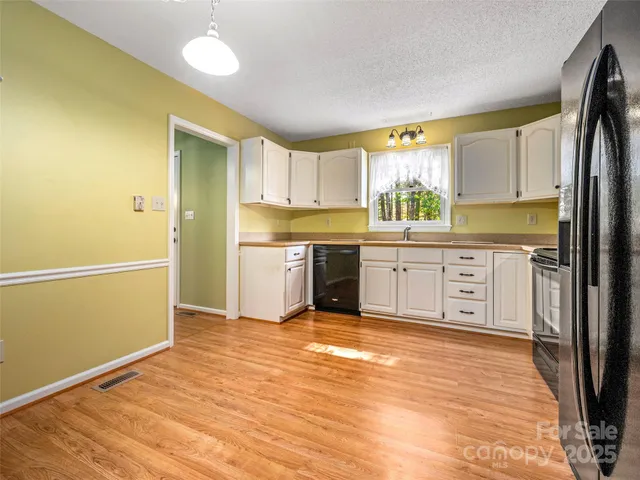 a kitchen with stainless steel appliances granite countertop a refrigerator a sink dishwasher and white cabinets with wooden floor