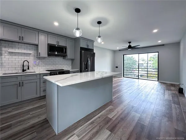 a kitchen with stainless steel appliances a microwave a sink dishwasher a refrigerator and white cabinets with wooden floor