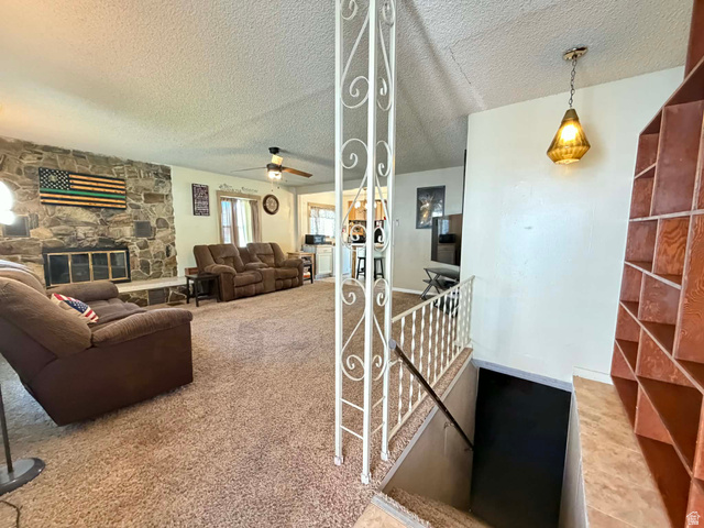 156 D Street Helper, UT 84526 - Photo 6 of 24 Carpeted living room with a stone fireplace, a textured ceiling, and a ceiling fan