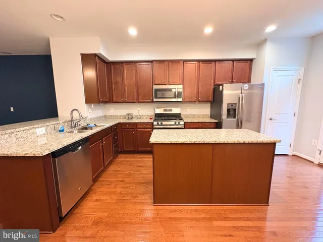 a large kitchen with stainless steel appliances kitchen island granite countertop a stove a sink dishwasher and a refrigerator with wooden floor