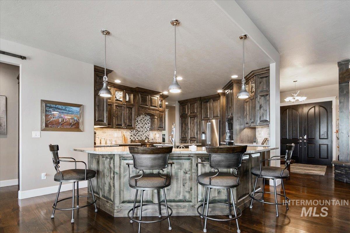24053 Pheasant Ridge Court Middleton, ID 83644 - Photo 12 of 50 Kitchen with light stone countertops, dark wood finish cabinetry, a chandelier, and a breakfast bar area