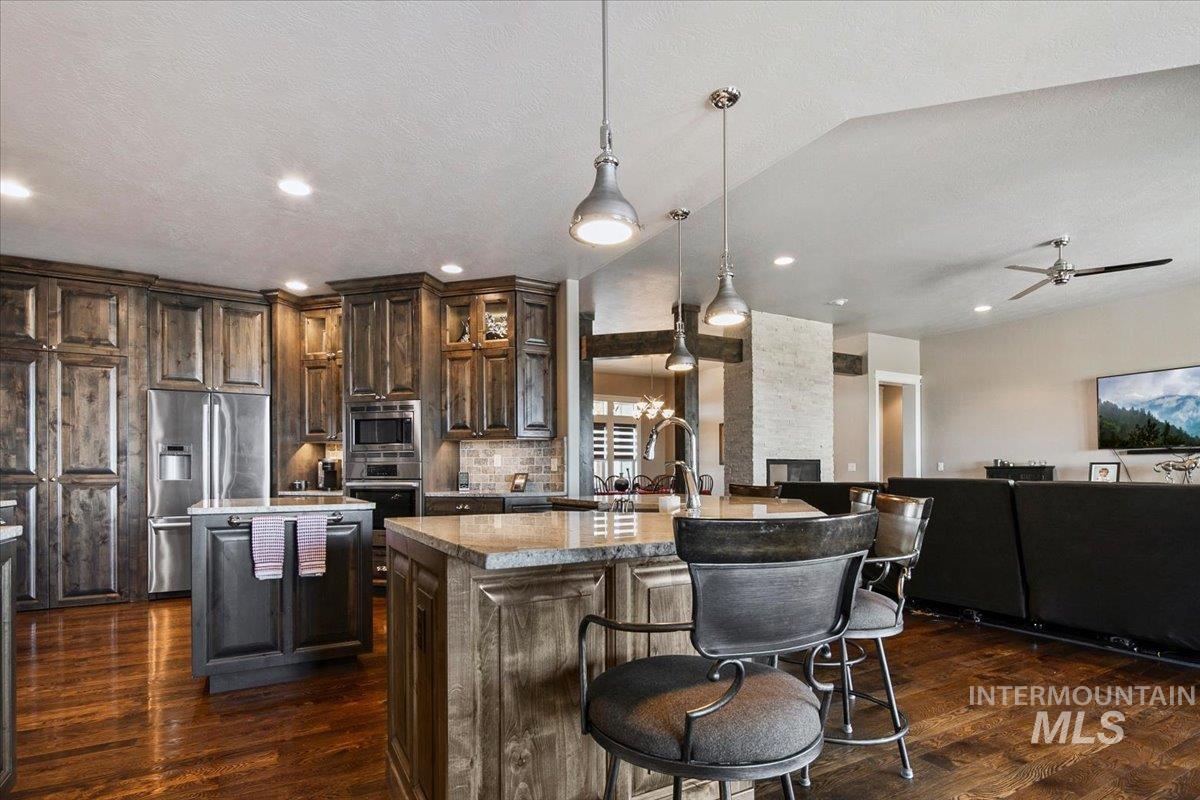 24053 Pheasant Ridge Court Middleton, ID 83644 - Photo 13 of 50 Kitchen featuring an island with sink, stainless steel appliances, dark wood finish cabinets, dark wood-style floors, and a textured ceiling