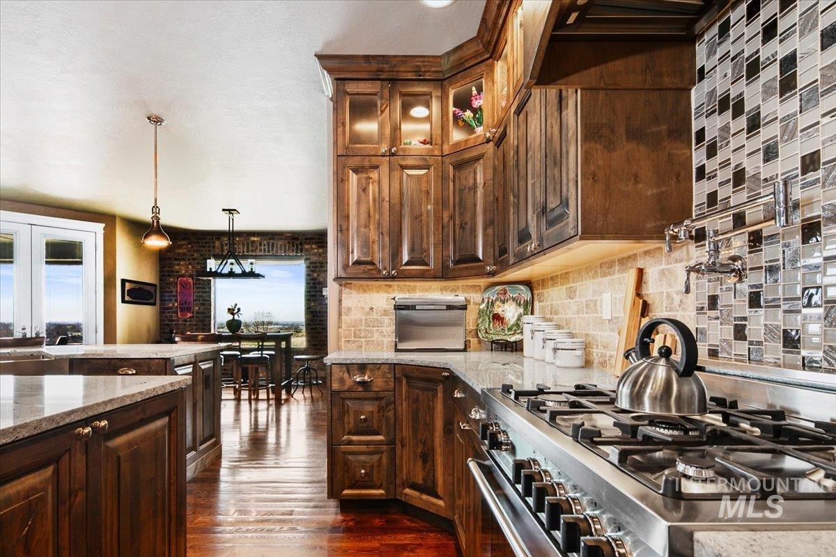 24053 Pheasant Ridge Court Middleton, ID 83644 - Photo 14 of 50 Kitchen with stainless steel stove, light stone countertops, dark wood-style floors, backsplash, and glass insert cabinets