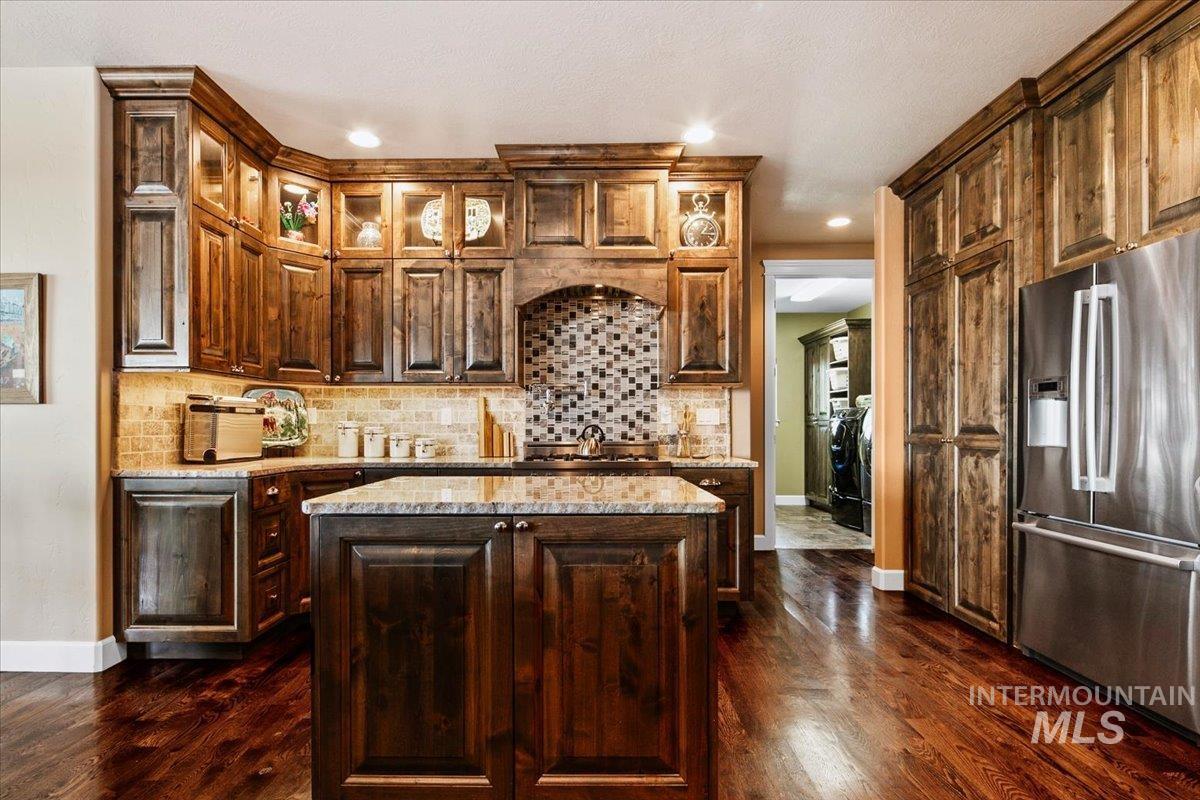 24053 Pheasant Ridge Court Middleton, ID 83644 - Photo 15 of 50 Kitchen with stainless steel fridge, decorative backsplash, a kitchen island, glass fronted cabinets, and dark wood-type flooring