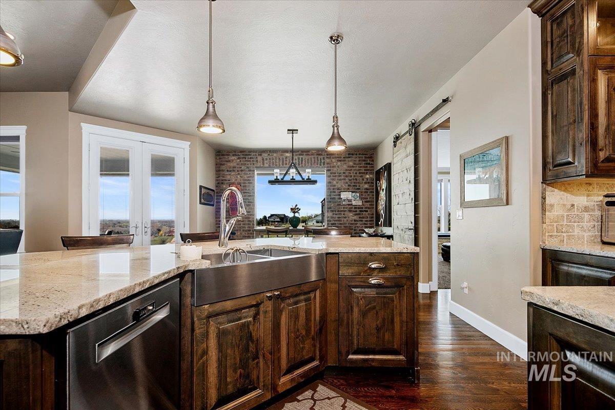24053 Pheasant Ridge Court Middleton, ID 83644 - Photo 16 of 50 Kitchen with dark wood finish cabinetry, dishwasher, dark wood-style floors, light stone counters, and brick wall