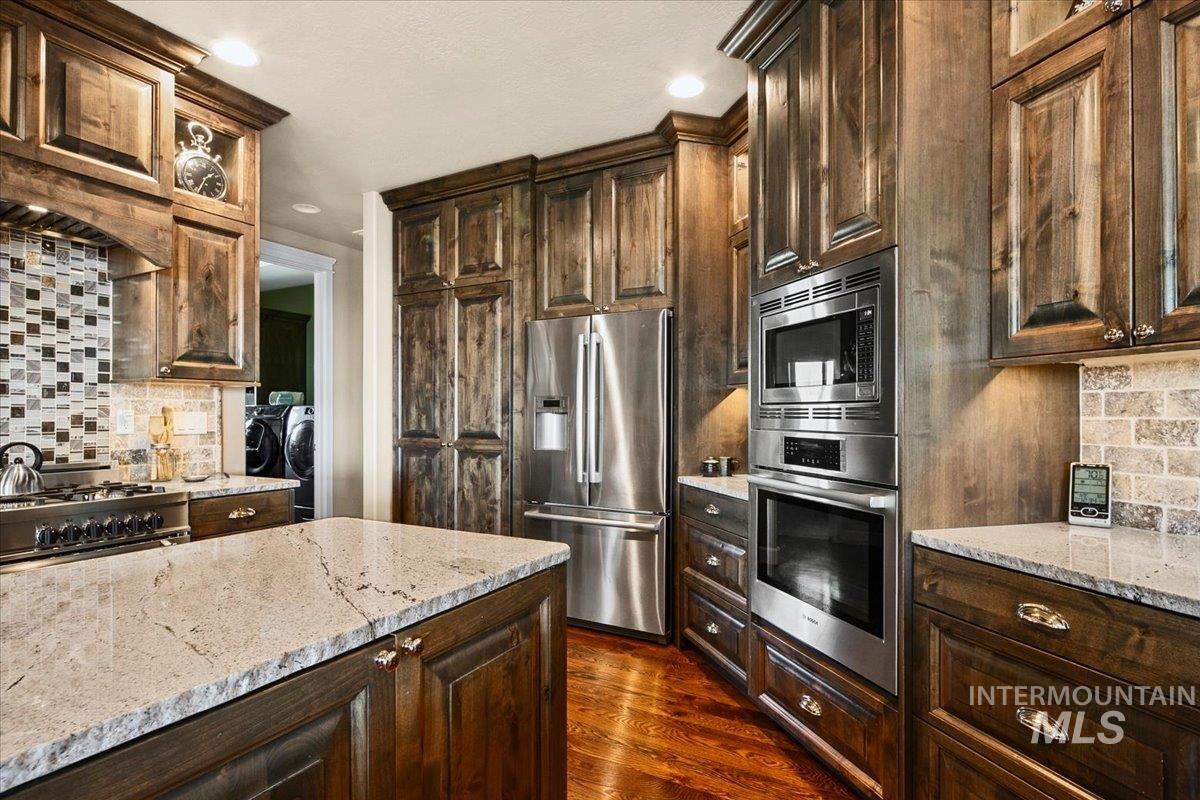 24053 Pheasant Ridge Court Middleton, ID 83644 - Photo 28 of 50 Kitchen featuring backsplash, stainless steel appliances, dark wood finish cabinetry, independent washer and dryer, and light stone countertops