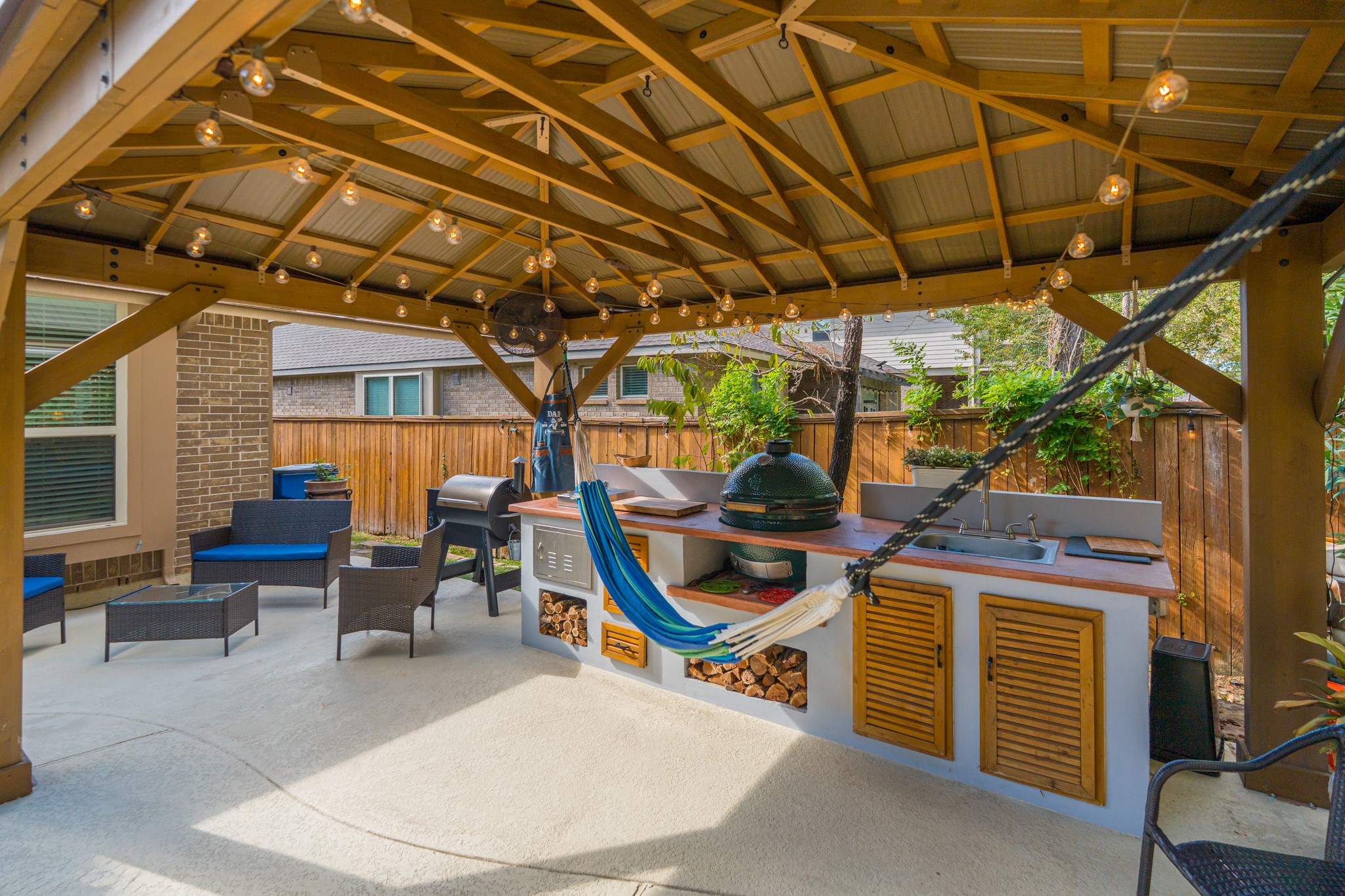 30 Fury Ranch Place The Woodlands, TX 77375 - Photo 47 of 47 This photo showcases a stylish outdoor patio with a wooden pergola, string lights, and a fully equipped kitchen area, including a grill and sink. The space features comfortable seating and a hammock, perfect for relaxation and entertaining.
