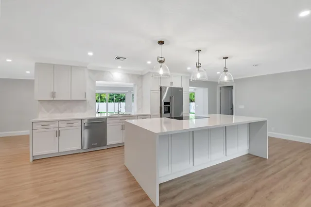 a large white kitchen with kitchen island a sink wooden floor and stainless steel appliances