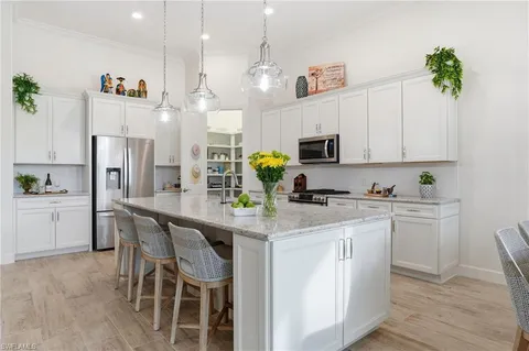 a kitchen with stainless steel appliances kitchen island granite countertop a refrigerator a stove a sink dishwasher and white cabinets with wooden floor