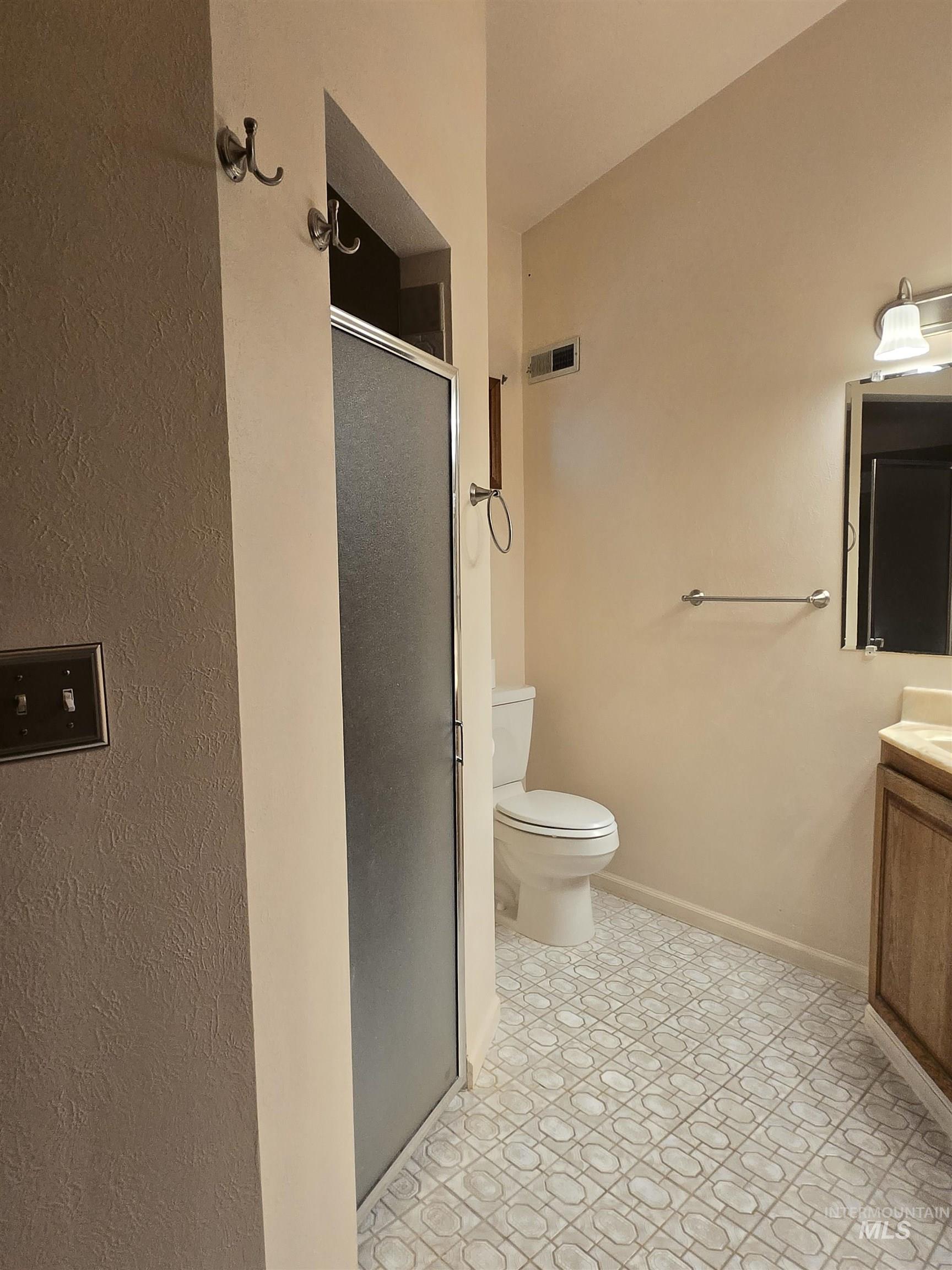 12050 West Hidden Valley Rim Road Boise, ID 83709 - Photo 13 of 39 Bathroom featuring a frosted glass shower enclosure, patterned floor tiles, and a vanity with a light wood-finish cabinet