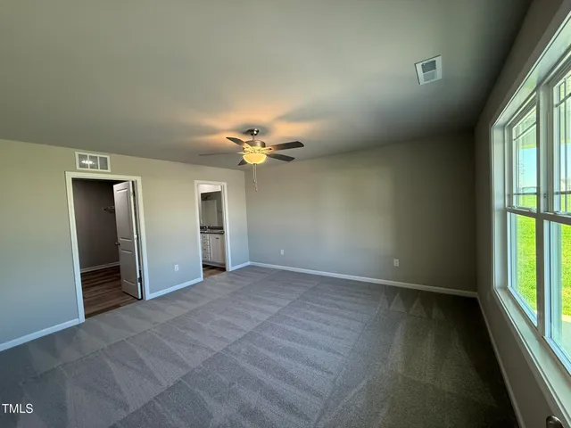 an empty room with chandelier fan and windows