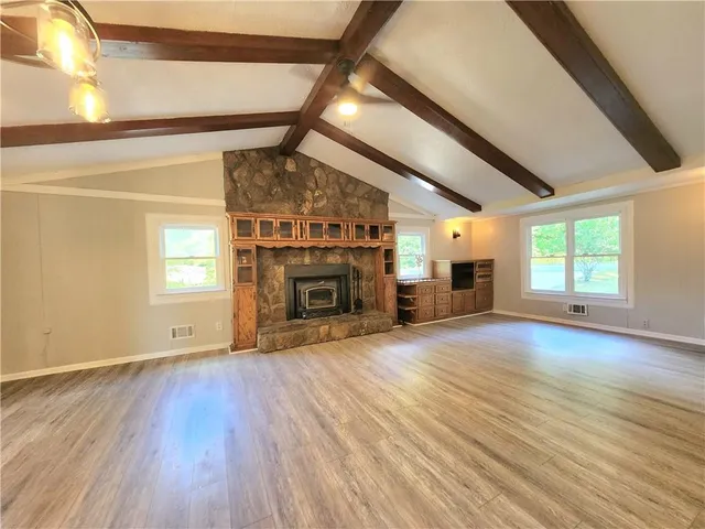 an empty room with wooden floor fireplace and windows