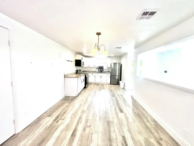 a large kitchen with granite countertop a stove top oven a sink dishwasher and white cabinets with wooden floor