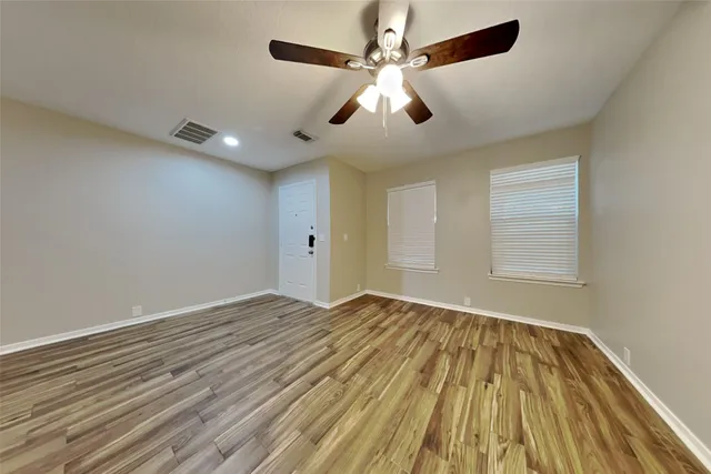 a view of an empty room with wooden floor and a ceiling fan