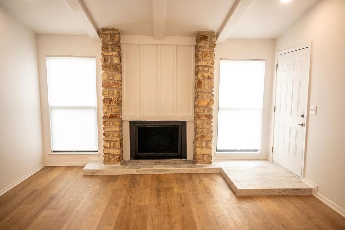 an empty room with wooden floor fireplace and windows