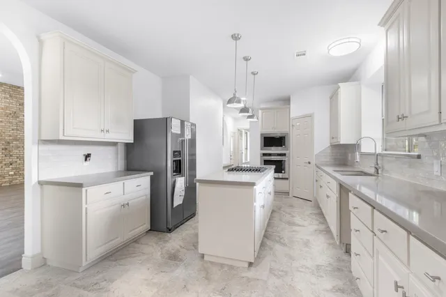 a large kitchen with stainless steel appliances kitchen island granite countertop a refrigerator a sink dishwasher a stove and white cabinets with wooden floor