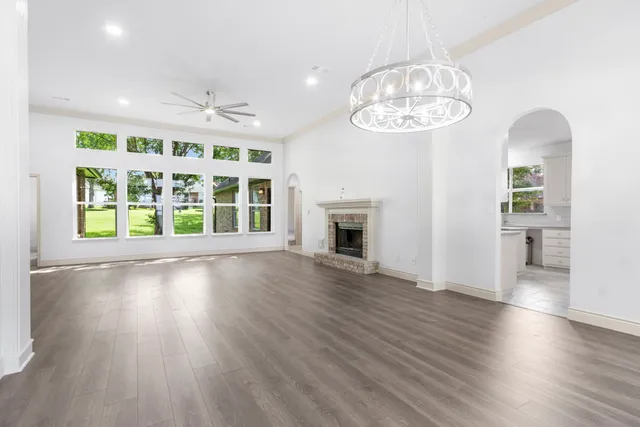 an empty room with wooden floor a chandelier a fireplace and windows