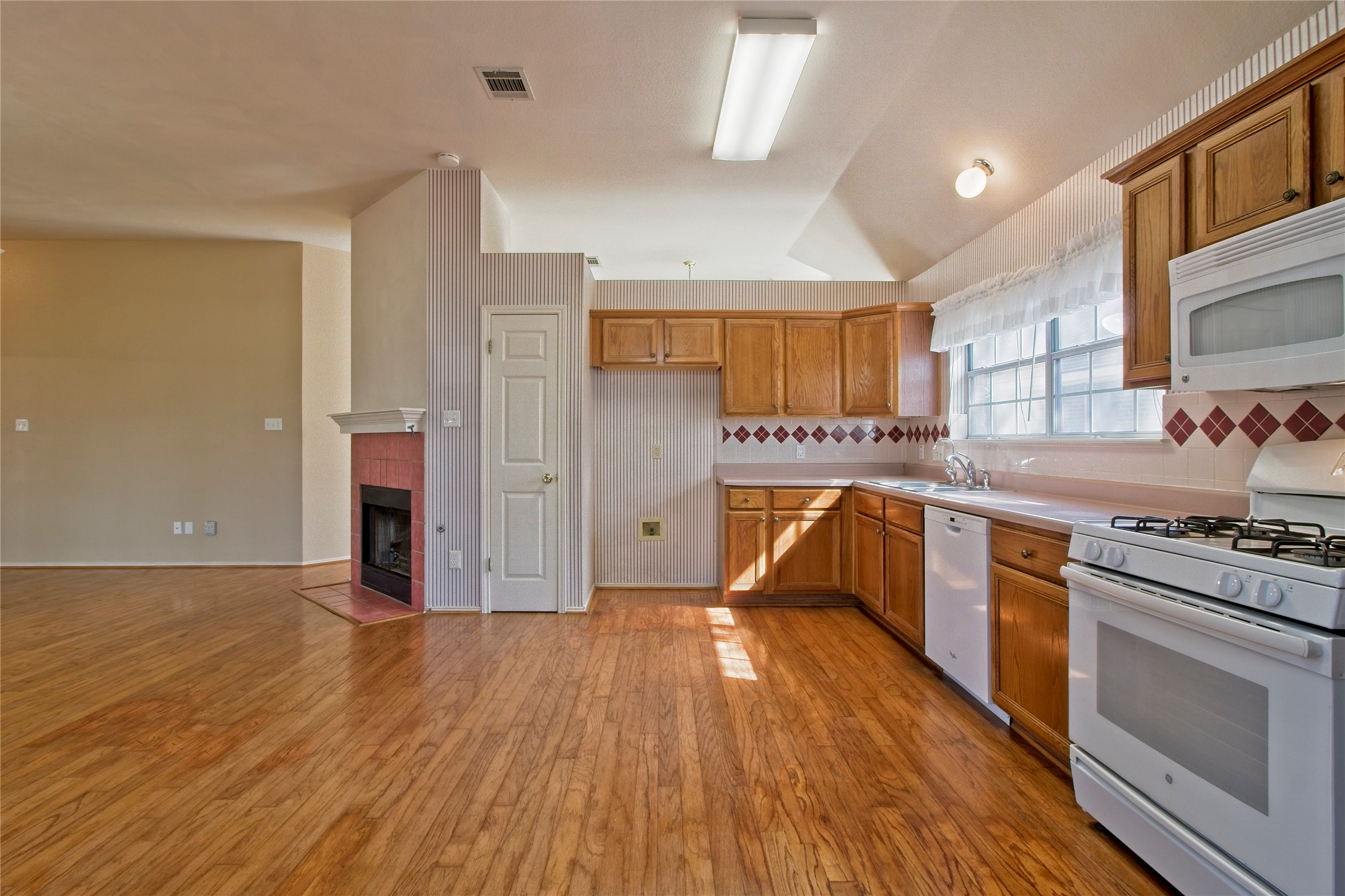 108 Rio Vista Drive Georgetown, TX 78626 - Photo 11 of 36 Kitchen with white appliances, light countertops, light wood-style floors, wood finish cabinetry, and a tiled fireplace