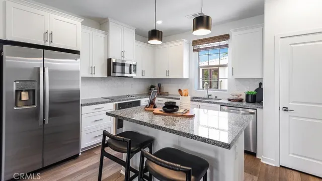 a kitchen with stainless steel appliances granite countertop a sink a stove a refrigerator and island with wooden floor