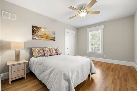 a bedroom with a bed and a lamp on dresser with wooden floor