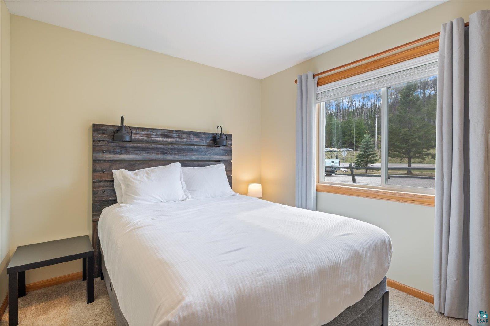 6266 Giants Ridge Road Biwabik, MN 55705 - Photo 25 of 37 Bedroom featuring a rustic wood-finish headboard with integrated sconce lighting, neutral wall paint, and a large window with wood-finish trim