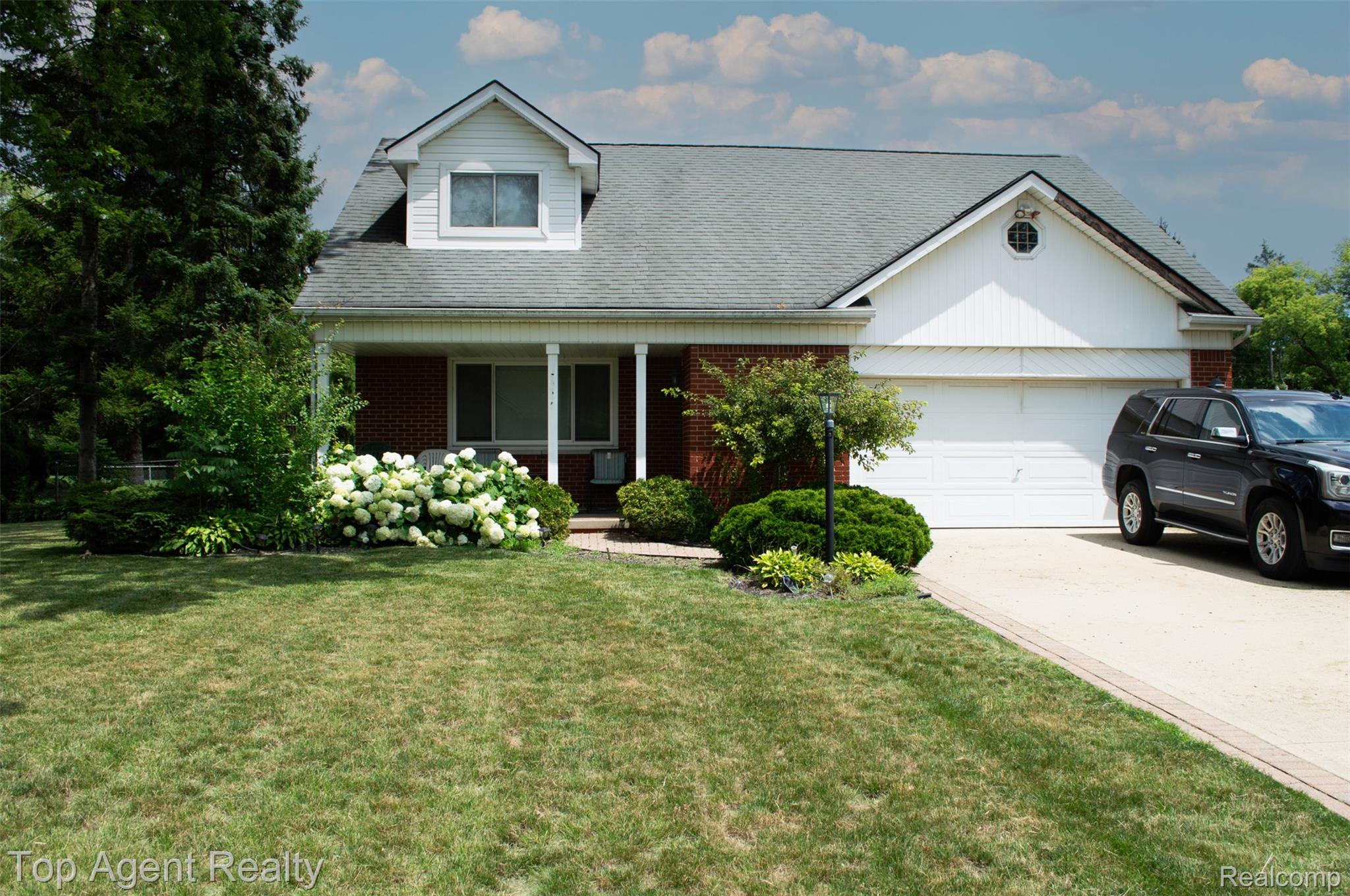 36218 Paddock Drive Clinton Township, MI 48035 - Photo 1 of 22 Brick and siding exterior featuring a covered porch with white columns, an attached two-car garage, and a dormer window