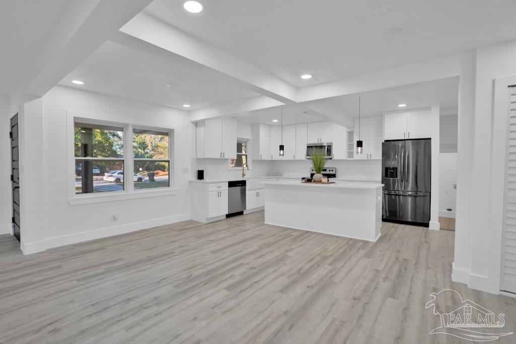 a large white kitchen with stainless steel appliances kitchen island a large counter top and a wooden floors