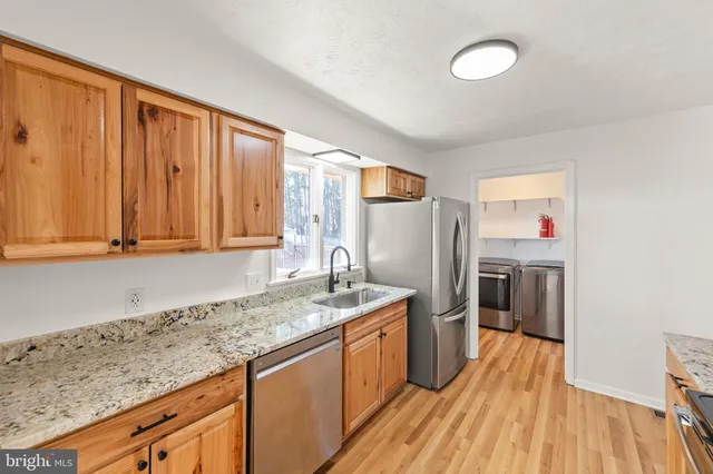 a kitchen with stainless steel appliances granite countertop a refrigerator a sink dishwasher and wooden cabinets with wooden floor